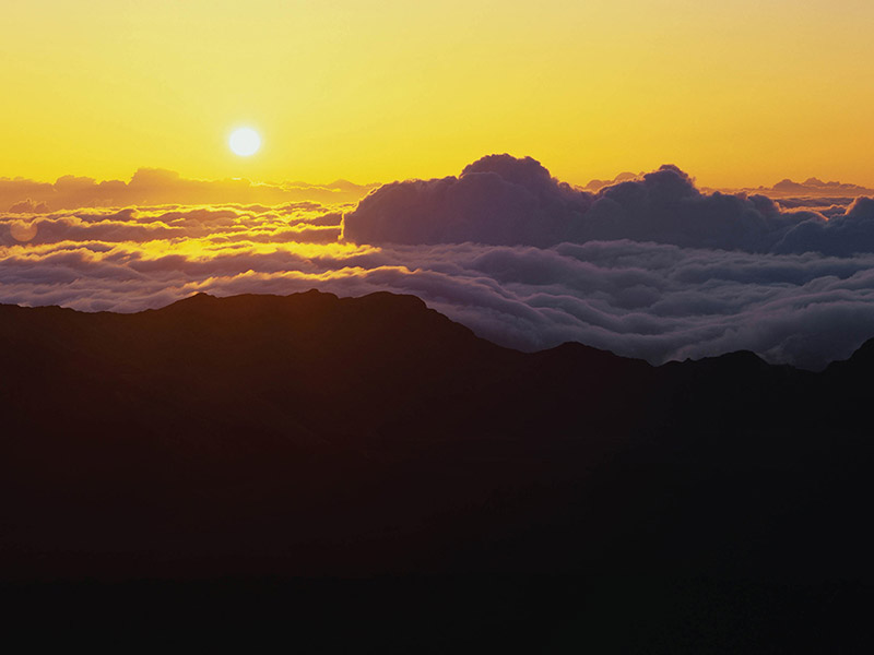 The sun rising over low clouds and the crater of Maui's Mount Haleakala