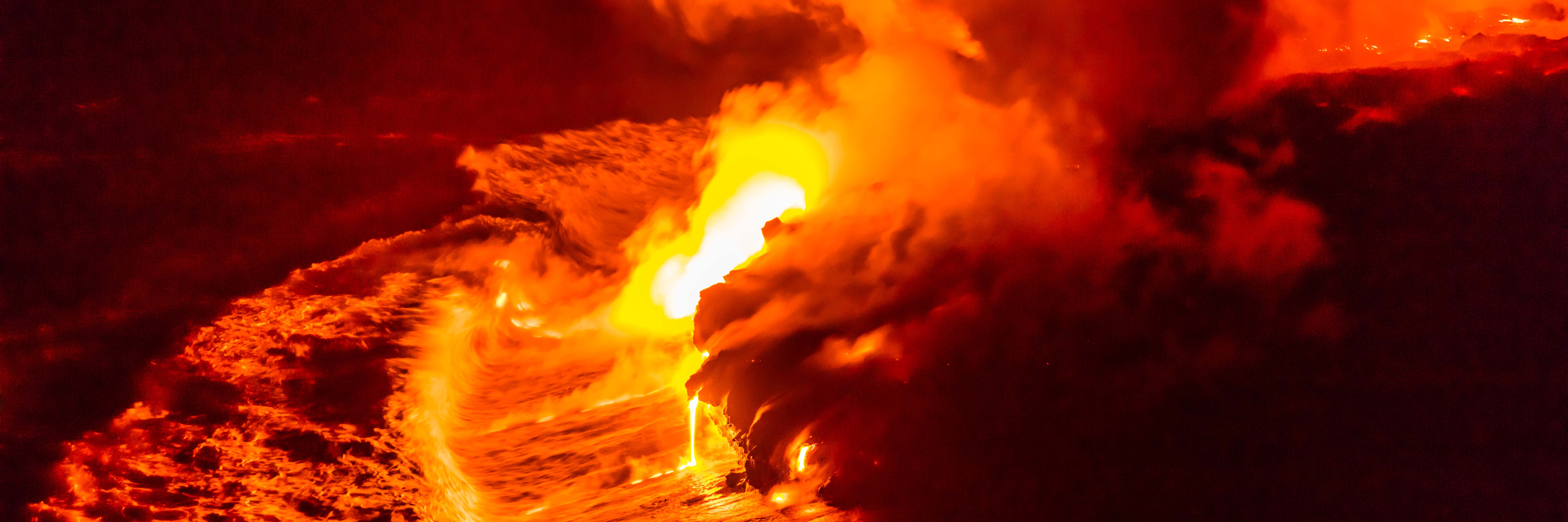 Lava flow falling in ocean waves in Hawaii from Hawaiian Kilauea volcano at night. Molten lava washed by the sea water crashing in, Big Island, USA.