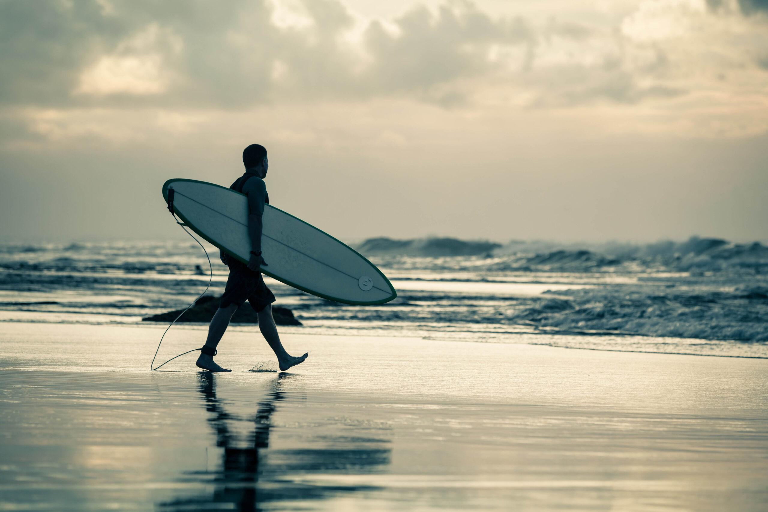 silhouette of a surfer walking to the ocean during sunset